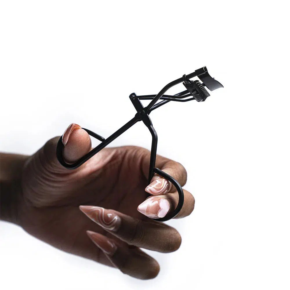 Close-up of a hand model holding black Lashy Cosmetics eyelash curlers open, viewed from the side.