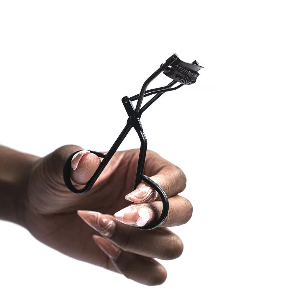Close-up of a hand model holding black Lashy Cosmetics eyelash curlers closed, viewed from the side.