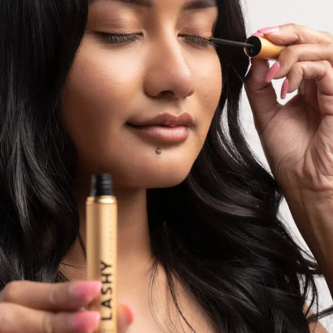 Close-up of a model with eyes closed applying Lashy Eyelash Serum with a gold applicator.