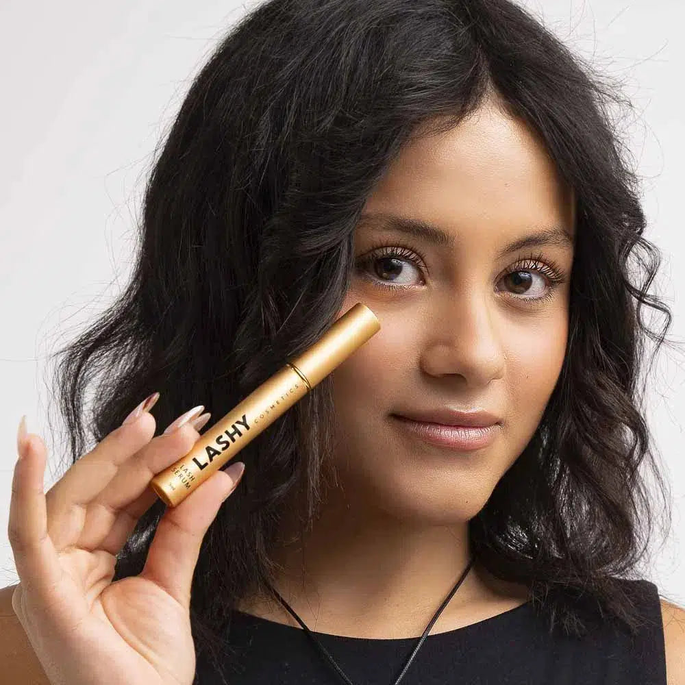 Close-up of a Lashy Cosmetics model smiling into the camera, holding the Lashy eyelash serum bottle in her right hand
