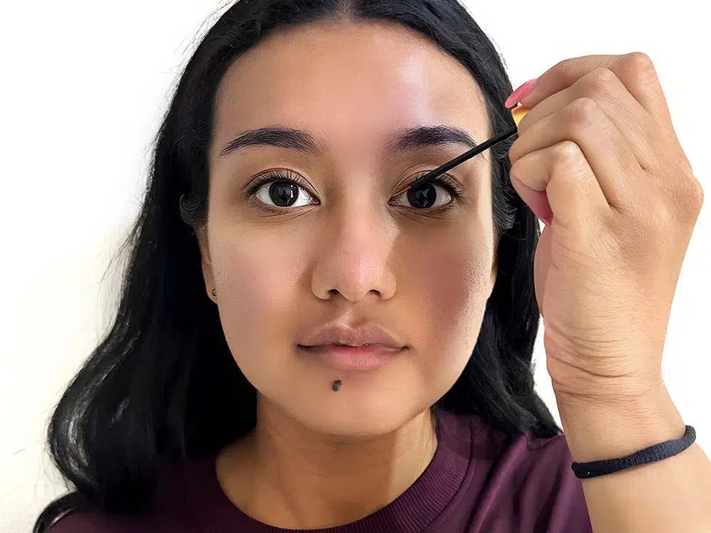 Close-up of a Lashy Cosmetics model looking into the camera, carefully applying eyelash growth serum as part of her nighttime beauty routine.