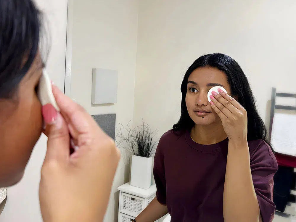 Lashy Cosmetics model removing makeup with a cotton pad in front of a mirror.